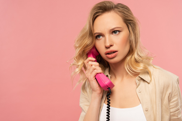 Serious blonde woman talking on retro telephone isolated on pink - Photo, Image