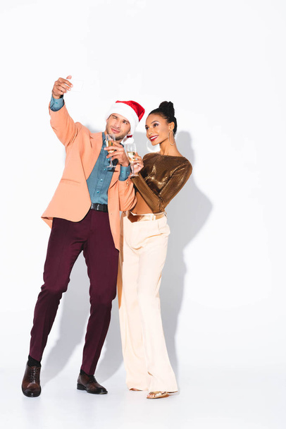 happy man in santa hat talking selfie with attractive african american girl on white  - Photo, Image