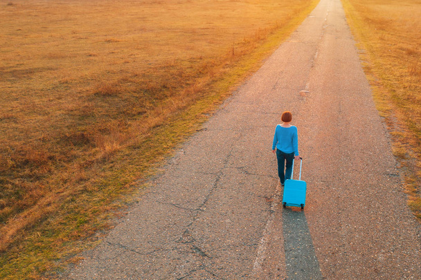 Sonbahar günbatımında seyahat valizlerini yolda taşıyan bir kadın. - Fotoğraf, Görsel