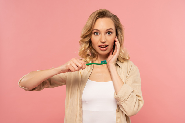 Shocked blonde woman holding toothbrush isolated on pink - Foto, immagini