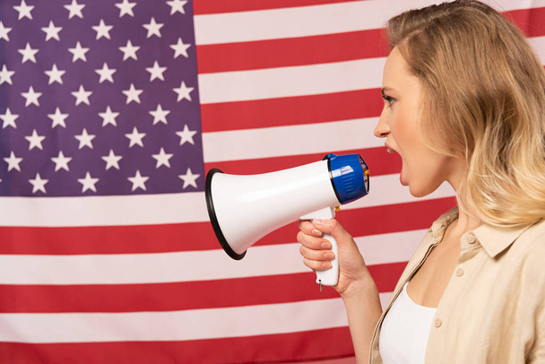 Νεαρή γυναίκα ουρλιάζει σε μεγάφωνο με αμερικανική σημαία στο βάθος - Φωτογραφία, εικόνα