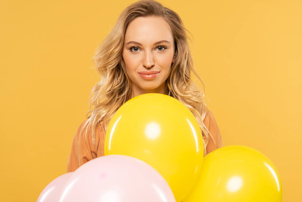 Smiling blonde woman holding balloons isolated on yellow - Foto, imagen
