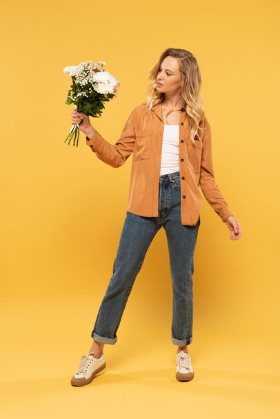 Attractive blonde woman holding bouquet on yellow background - Фото, зображення