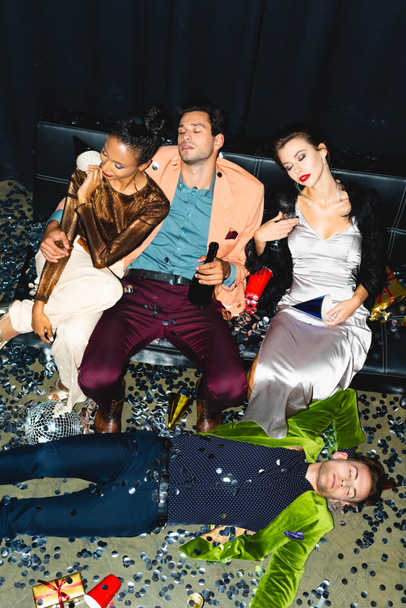 shora pohled unavených multikulturních přátel spících na pohovce v blízkosti diskotéky  - Fotografie, Obrázek