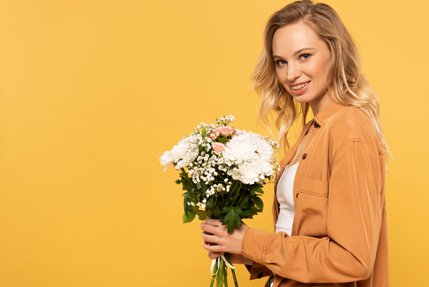 Side view of woman holding bouquet and smiling at camera isolated on yellow - Foto, Bild
