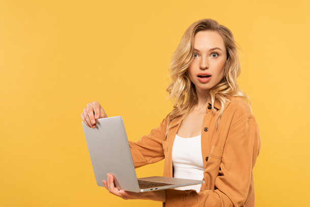 Opgewonden jonge vrouw houden laptop geïsoleerd op geel - Foto, afbeelding