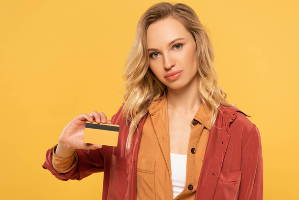 Attractive blonde woman holding credit card isolated on yellow - 写真・画像