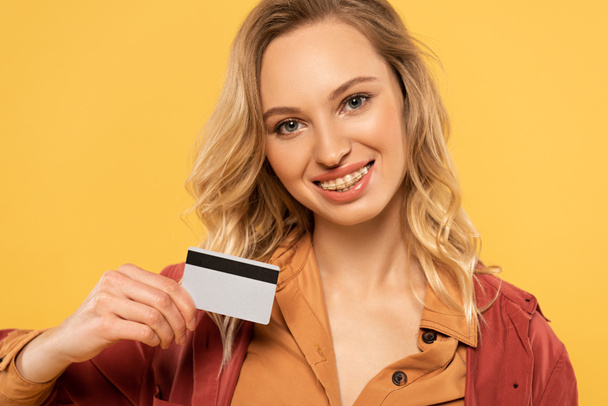 Smiling woman holding credit card isolated on yellow - Valokuva, kuva