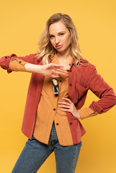 Blonde woman holding car keys and looking at camera isolated on yellow - Foto, immagini