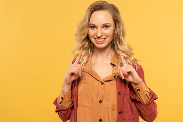Smiling woman pointing up with fingers isolated on yellow - Фото, зображення
