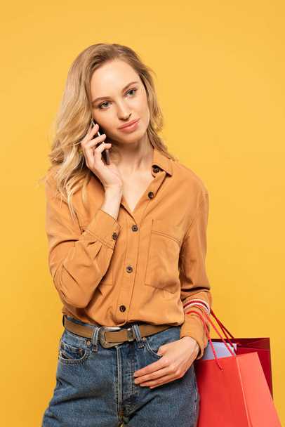 Femme blonde parlant sur smartphone et tenant des sacs à provisions isolés sur jaune
 - Photo, image