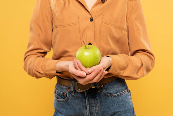 Vista ritagliata della donna che tiene mela verde isolata sul giallo
 - Foto, immagini