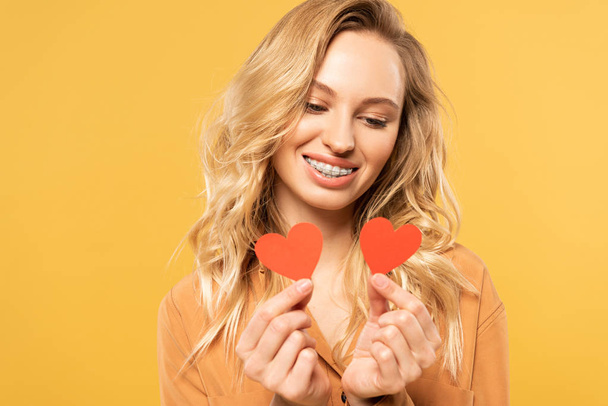 Smiling blonde woman looking at paper hearts isolated on yellow - Φωτογραφία, εικόνα