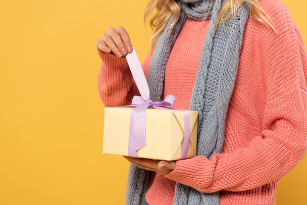 Обрізаний вид жінки розв'язати стрічку на подарунковій коробці ізольовано на жовтому
 - Фото, зображення