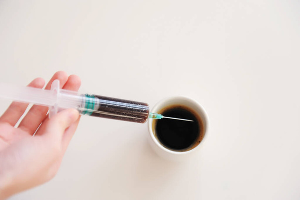Hand pflückt Espresso in eine medizinische Spritze. Symbol der Koffeinsucht. weißer Hintergrund - Foto, Bild