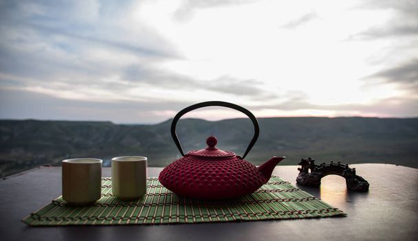 Концепция чая. Культура японской чайной церемонии восточный напиток. Чайник и чашки на столе с бамбуковыми листьями на закате
 - Фото, изображение