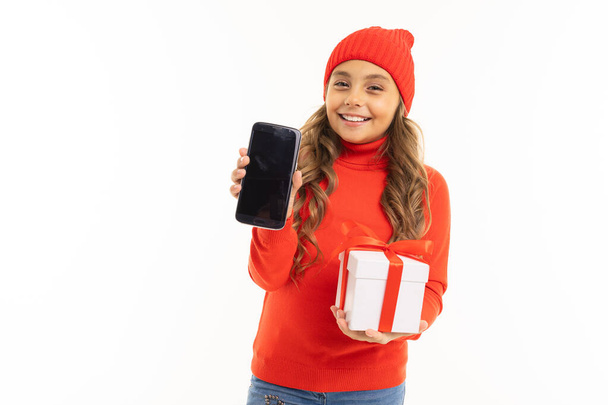 mignonne petite fille en pull rouge et chapeau posant avec boîte cadeau et téléphone mobile sur fond blanc
  - Photo, image