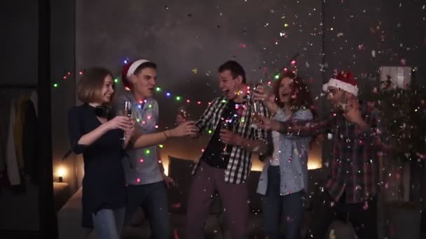 Colorful celebration of Christmas and New year. Festive party, group of five clink glasses with champagne after one guy explodes the confetti stick. Happy celebration together with close friends at - Footage, Video