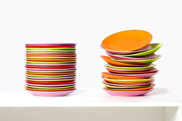 die Stapel mehrfarbiger Teller laugen auf einem weißen Tisch - Foto, Bild