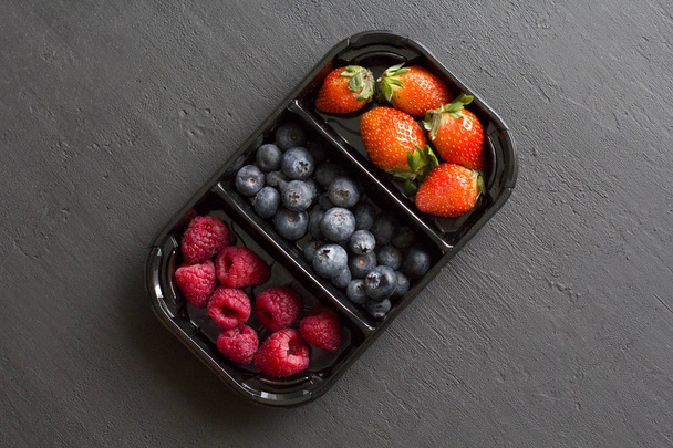 Fraises douces fraîches fraises, bleuets et framboises se trouvent dans le plateau, boîte sur fond noir. Concept de récolte. Mélanger les baies sur un fond noir. Fruits avec espace de copie pour le texte
 - Photo, image