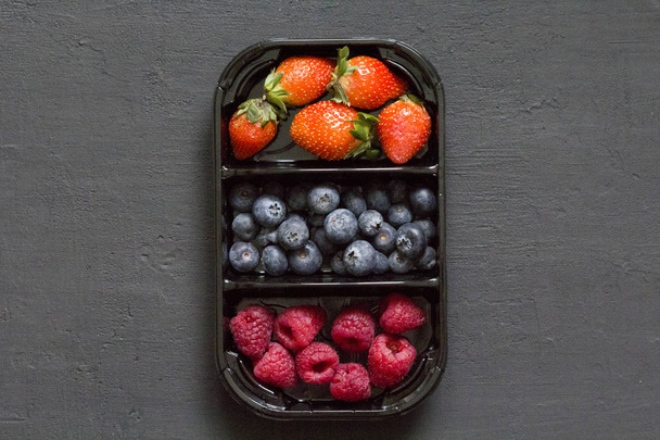 Fraises douces fraîches fraises, bleuets et framboises se trouvent dans le plateau, boîte sur fond noir. Concept de récolte. Mélanger les baies sur un fond noir. Fruits avec espace de copie pour le texte
 - Photo, image