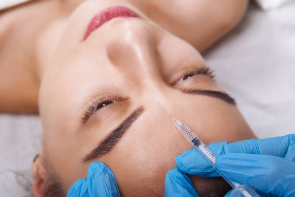 Closeup Retrato de mulher branca jovem recebendo injeção cosmética de botox na testa. Pessoas, cosmetologia, cirurgia plástica e conceito de beleza
. - Foto, Imagem
