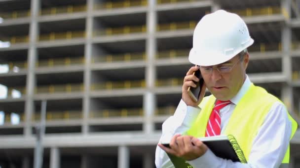 Inżynier budowlany w koszuli i krawacie z kaskiem i kamizelką pracuje na budowie, rozmawia przez telefon. Pojęcie osób pracujących w przemyśle - Materiał filmowy, wideo