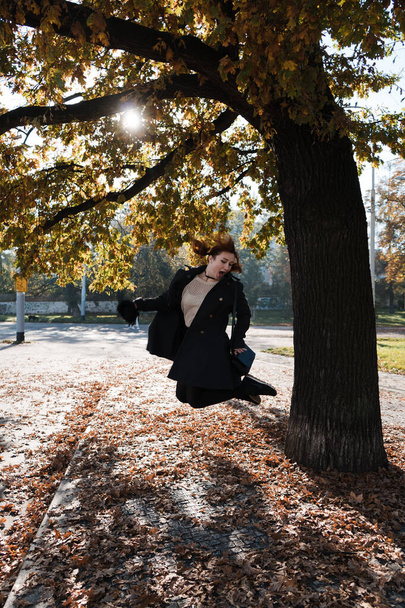 Mujer pelirroja feliz lanzando y jugando con hojas de otoño comenzando una nueva vida en Praga
 - Foto, imagen