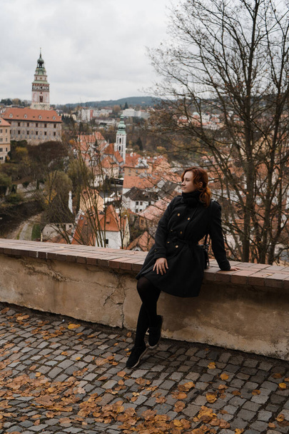 Redhead happy woman in Cesky Krumlov with a rooftop view over city centre, castle and Church of St. Vitus - Photo, image