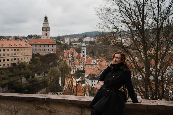 Pelirroja feliz mujer en Cesky Krumlov con una vista de la azotea sobre el centro de la ciudad, el castillo y la Iglesia de San Vito
 - Foto, Imagen