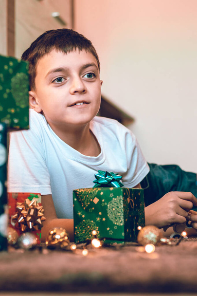 Νεαρό αγόρι ετοιμάζει δώρα για τα Χριστούγεννα. Ξεπακετάρω δώρα στο τραπέζι. Χειμερινές διακοπές γιορτάζουν έννοια. - Φωτογραφία, εικόνα