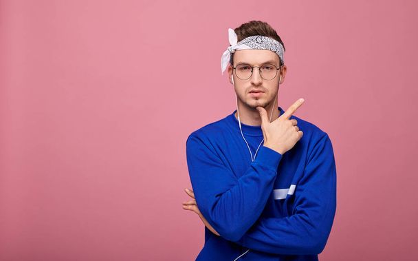 Confident guy in glasses in white bandanna and in blue jacket posing on pink background  - Foto, Imagen
