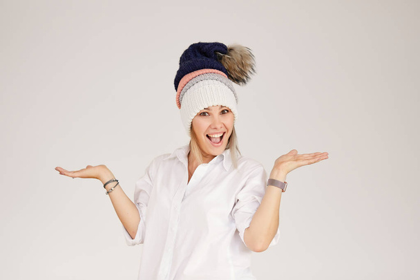 Portrait of happy young smiling woman wearing many colorful knitted hats over white background. Spreads her arms to the side and is surprised. Empty space for text. - Фото, зображення