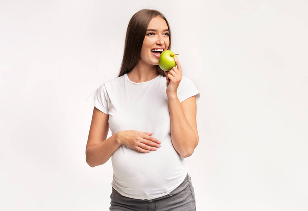 Pregnant Woman Eating Apple Posing Over White Studio Background - Foto, Imagem
