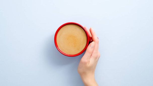 Female hand holding latte coffee cup on blue background. Flat lay, top view, overhead. - Foto, imagen