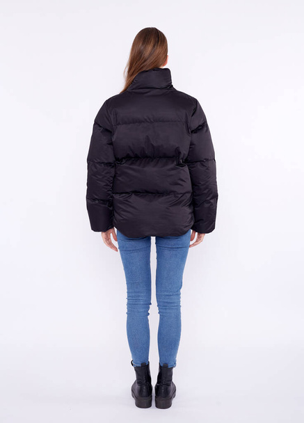 Young girl in a black down jacket and blue jeans isolated on a white background. - Photo, Image