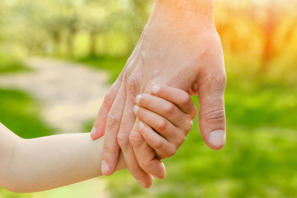 der Elternteil hält die Hand des Kindes mit einem glücklichen Hintergrund - Foto, Bild