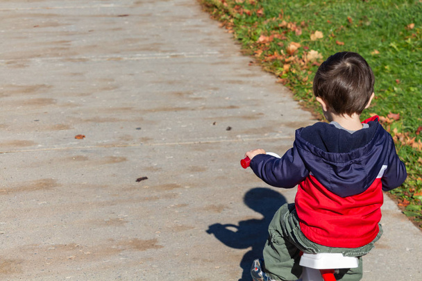 Το μικρό αγόρι τρέχει το τρίκυκλό του μακριά σε μια πλαϊνή βόλτα - Φωτογραφία, εικόνα