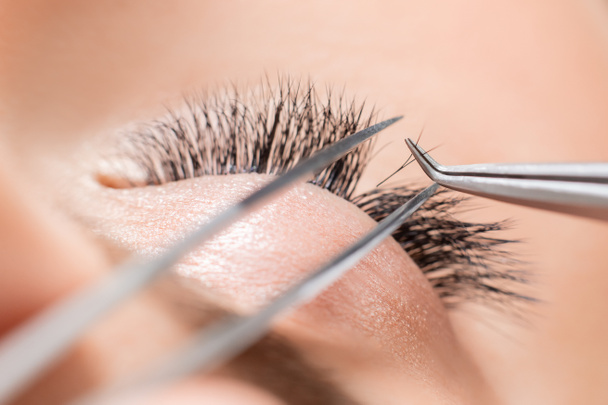 Eyelash extension procedure. Master tweezers sets fake lashes on beautiful woman - Φωτογραφία, εικόνα