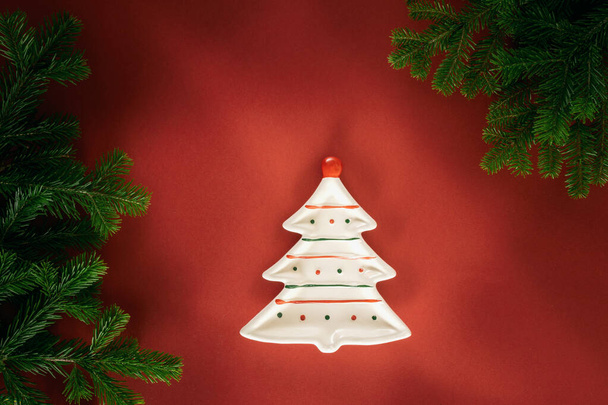 Christmas composition. A plate in the form of a Christmas tree and fir branches on a red background. Flat lay, top view, copy space. - Fotografie, Obrázek