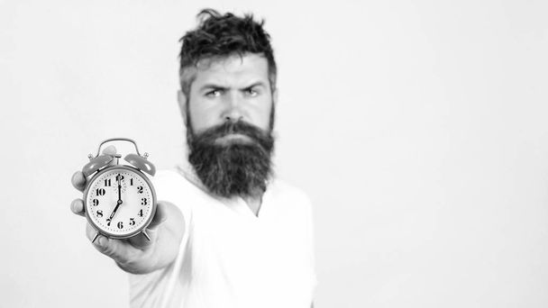 髭の男が白い壁に目覚まし時計を持っている。時計に集中しろ季節の時間を変えろ時間管理 - 写真・画像