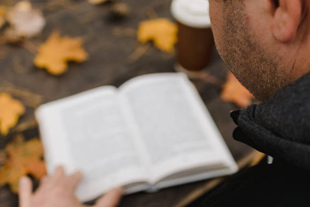 férfi nő olvas egy könyvet az őszi parkban iszik elvitelre kávét. Közelkép a válla fölött, elmosódott. felülnézet, helyet takarít meg. Láttam a kezeit. Sötét retro stílusban - Fotó, kép