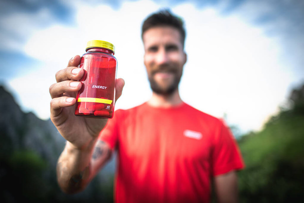 Bottle of energy capsules in the hands of sportsmen - Photo, Image