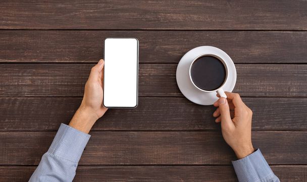 Man holding smartphone with blank screen and drinking coffee - Photo, Image