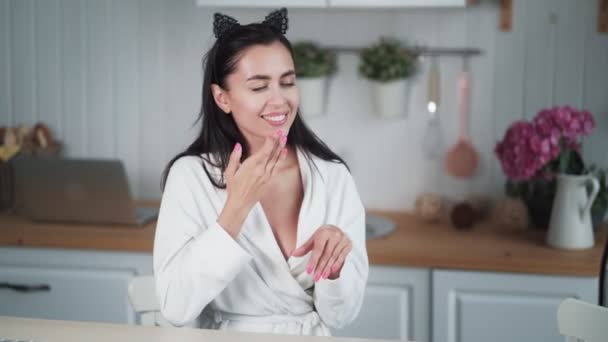 Portrait of woman in bathrobe applies cream on her face and does facial massage - Felvétel, videó
