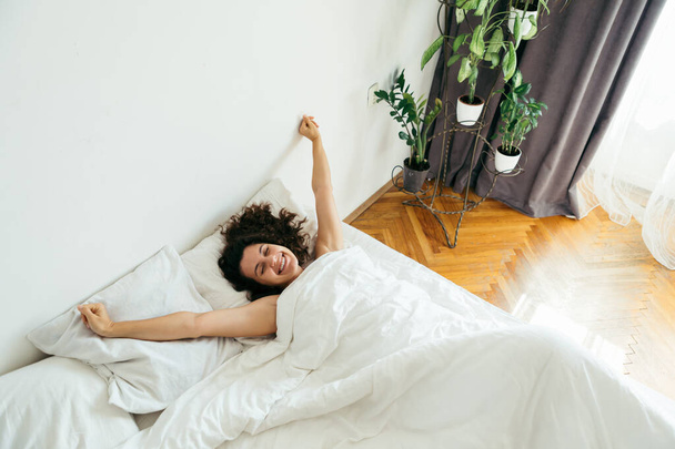 jovem mulher bonita na cama com lençóis brancos luz brilhante
 - Foto, Imagem