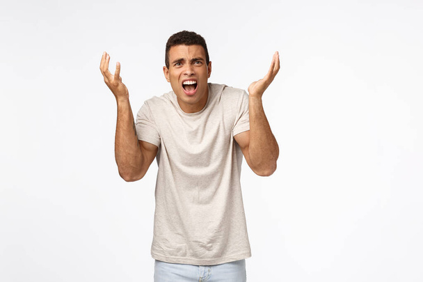 Disappointed and freak-out, bothered handsome man in t-shirt, raising hands up frustrated and displeased, arguing, complaining over unfair failure, losing competition, standing upset white background - Photo, Image