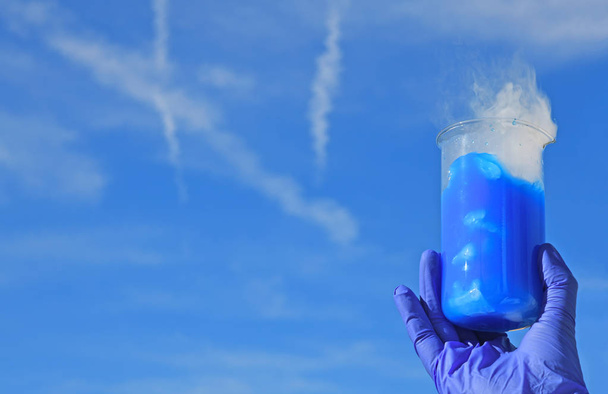 Witte rook komt uit een bekerglas met blauwe oplossing van fluoresceïne na toevoeging van droog ijs. Experiment met chemische demonstratie. - Foto, afbeelding