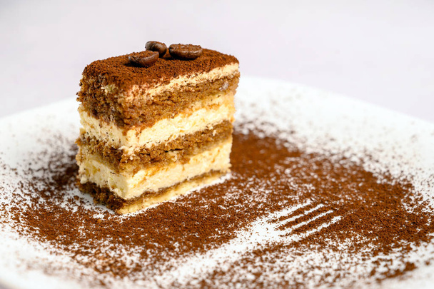 Fatia de bolo tiramisu decorado com grãos de café em cima em uma placa branca
 - Foto, Imagem