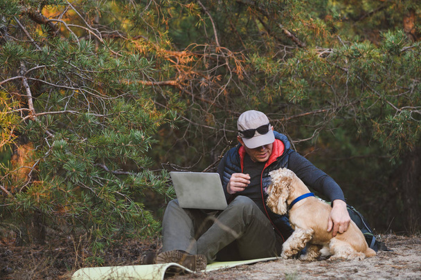 Пожилой турист с ноутбуком и собакой в лесу
 - Фото, изображение
